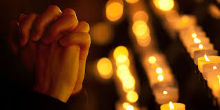 Folded hands before a row of candles