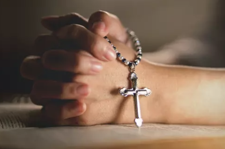 Hands holding a rosary over a book
